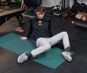 Dr. Jon dropping one knee inside while keeping his glute on the ground perfoming windshield wipers as one of our best mobility exercises to try